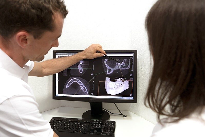 Dr. Dr. Marc Füßinger erklärt einer Patientin die Aufnahmen am Monitor